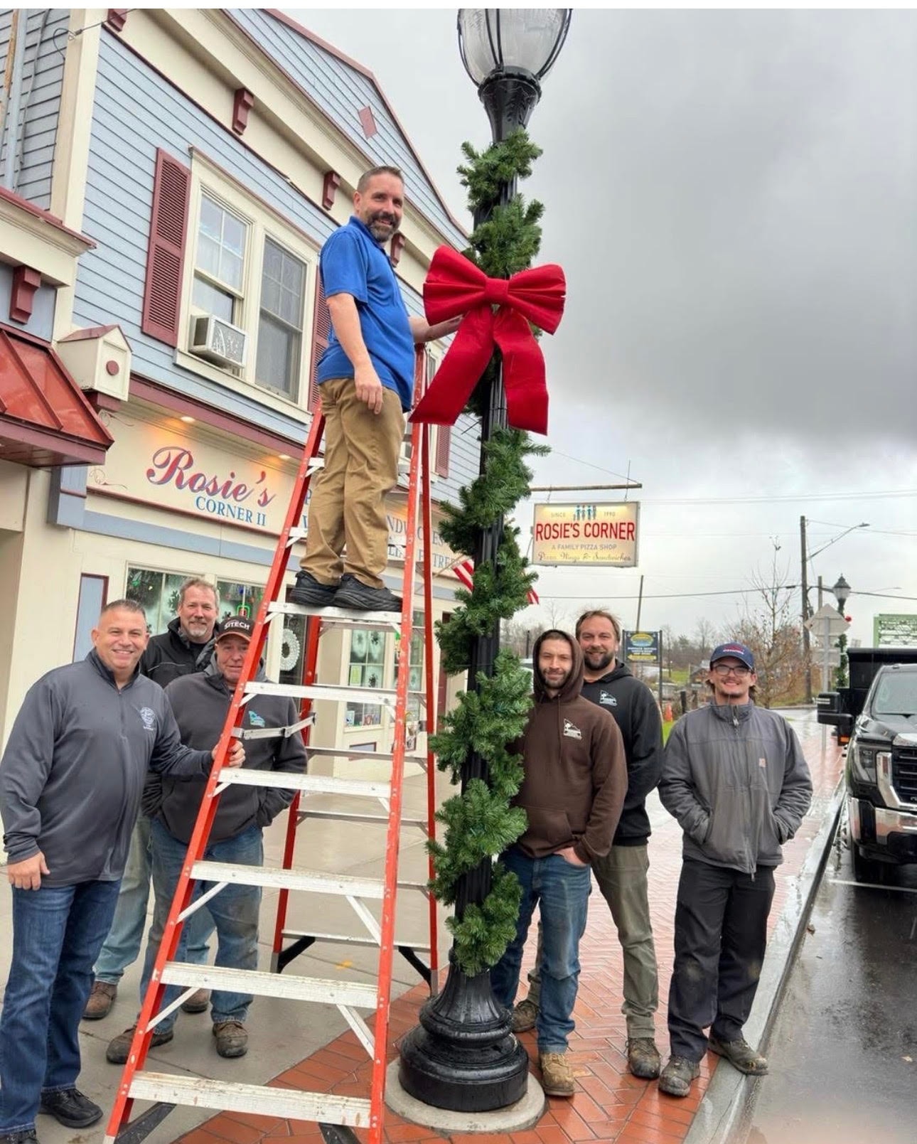 Team decorating street lamp with garland and red bow in Brewerton